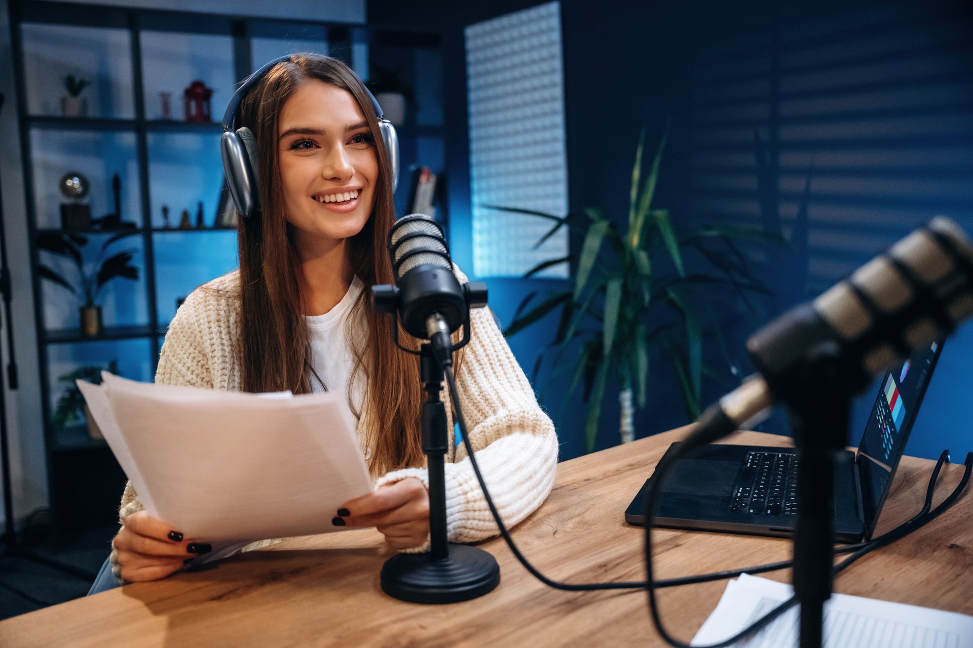 Vorderansicht, sitzend. Frau moderiert Radio-Podcast mit Mikrofon und Laptop
