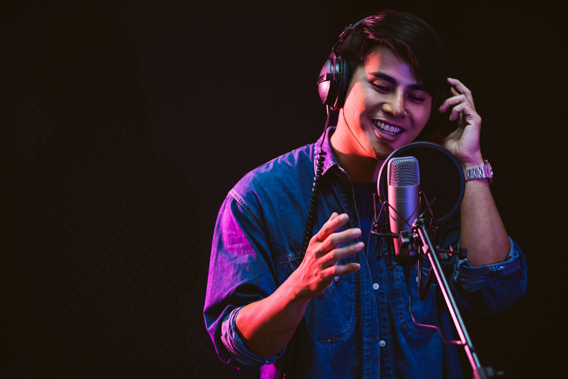 Asiatischer Sänger, der Songs mit einem Studiomikrofon und einem Popschild am Mikrofon mit Leidenschaft in einem Musikaufnahmestudio aufnimmt. Performance und Show im Musikbusiness. Fokus auf männliches Gesicht